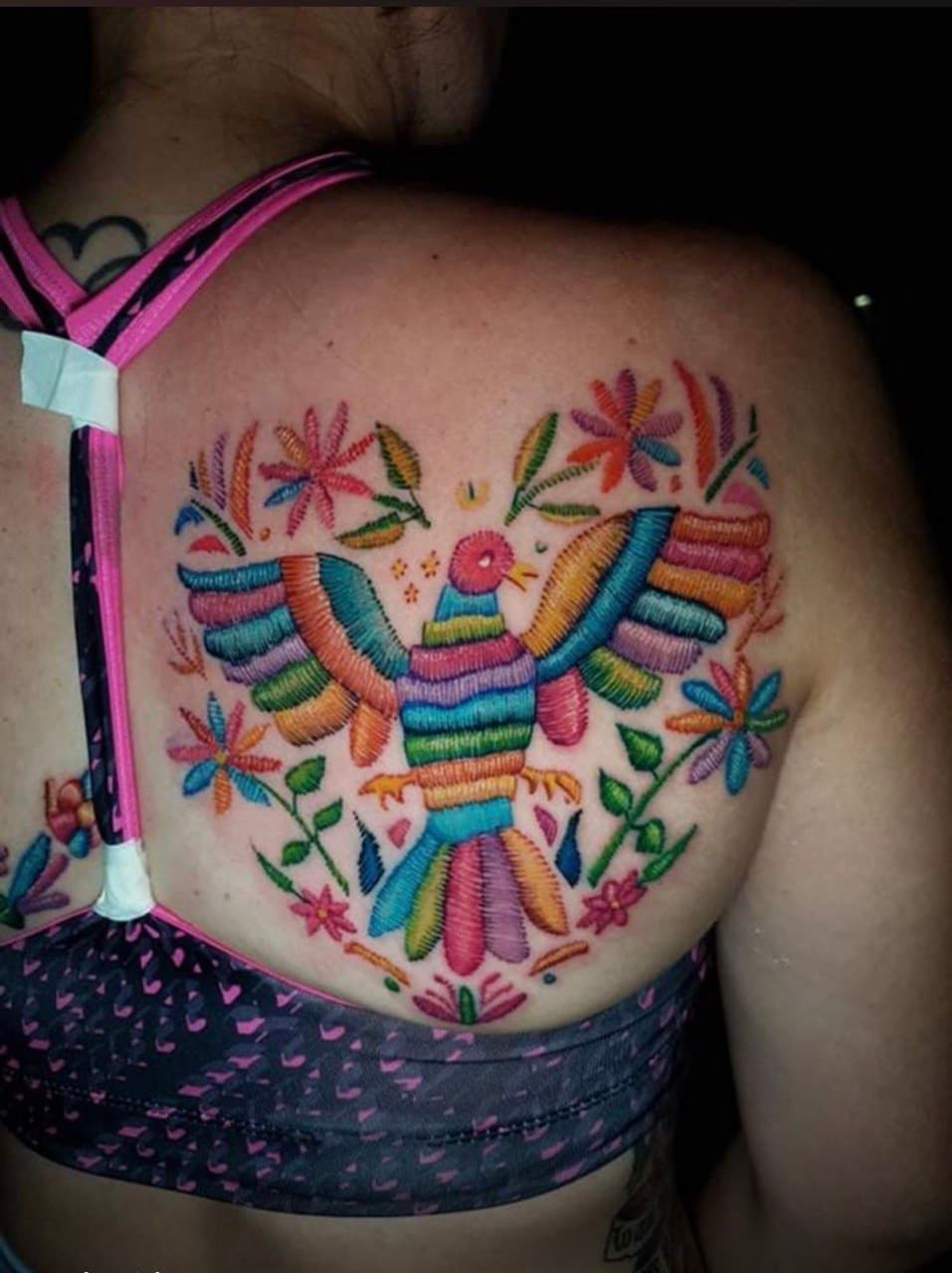 Colorful bird and floral tattoo across an upper back