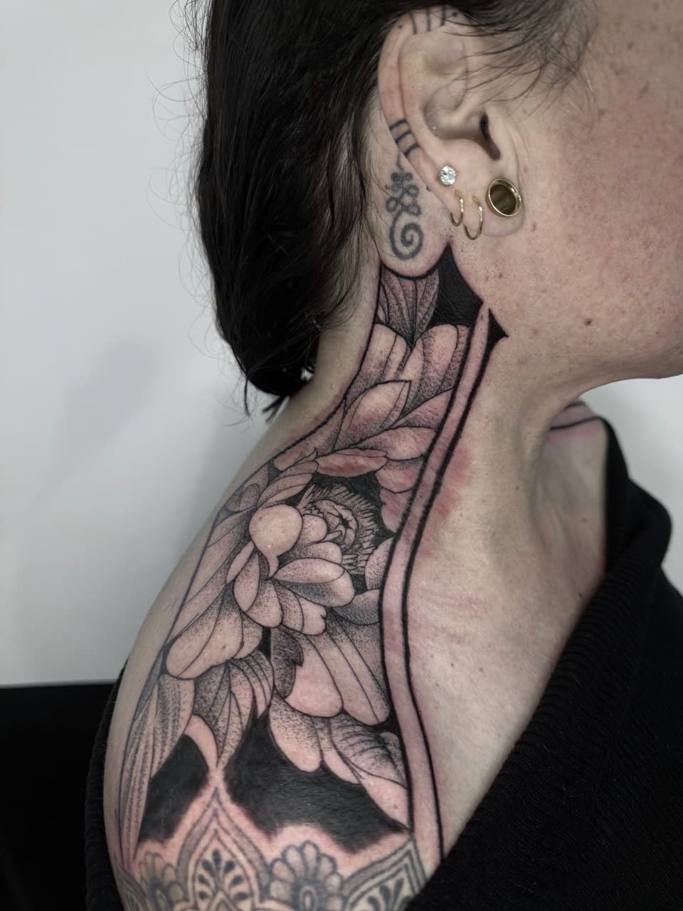 Black and grey floral tattoo along a neck and shoulder