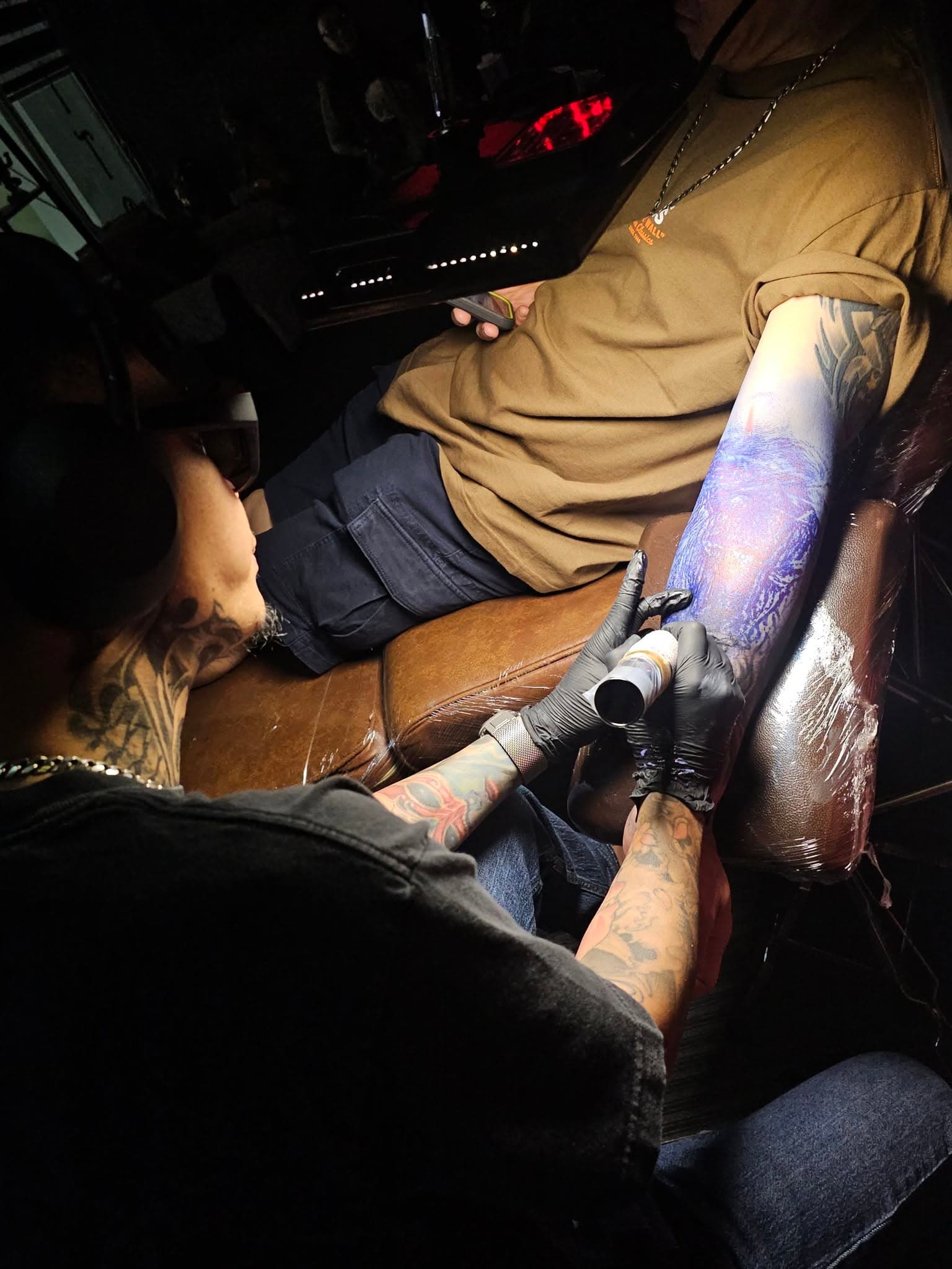 Tattoo artist working on a forearm under a focused task light